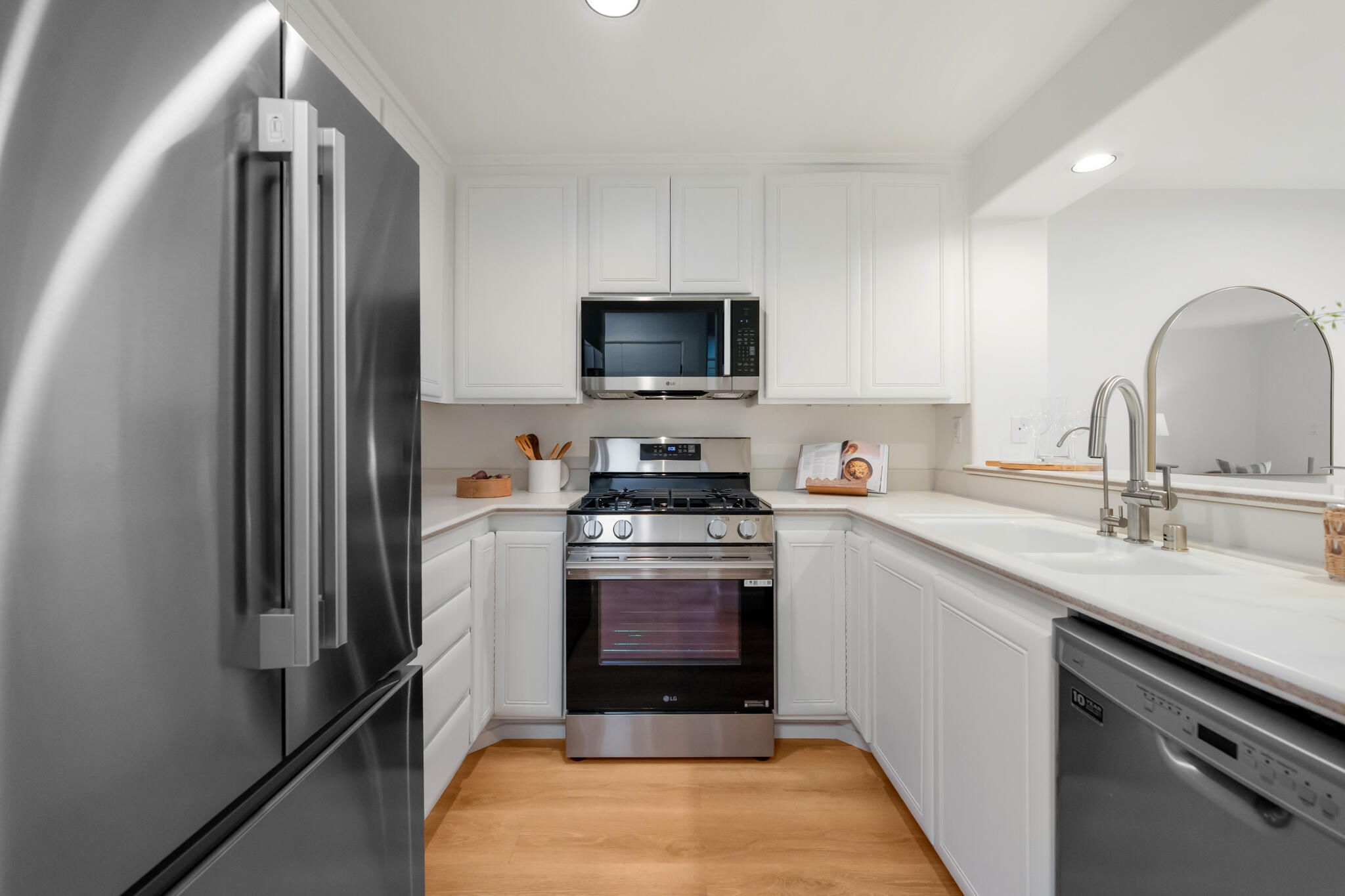Bright white kitchen with stainless-steel appliances, a double-basin sink, and warm wood flooring.