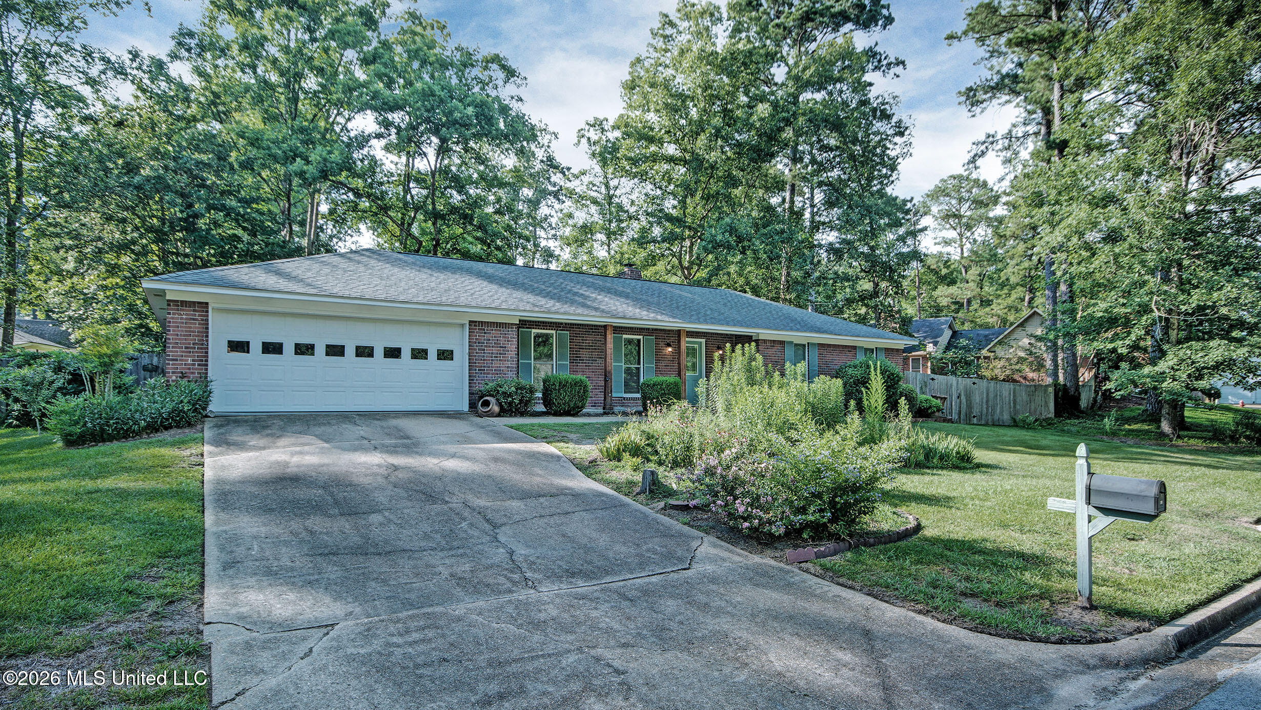 Single-story brick home with an attached garage, broad driveway, and landscaped front garden.