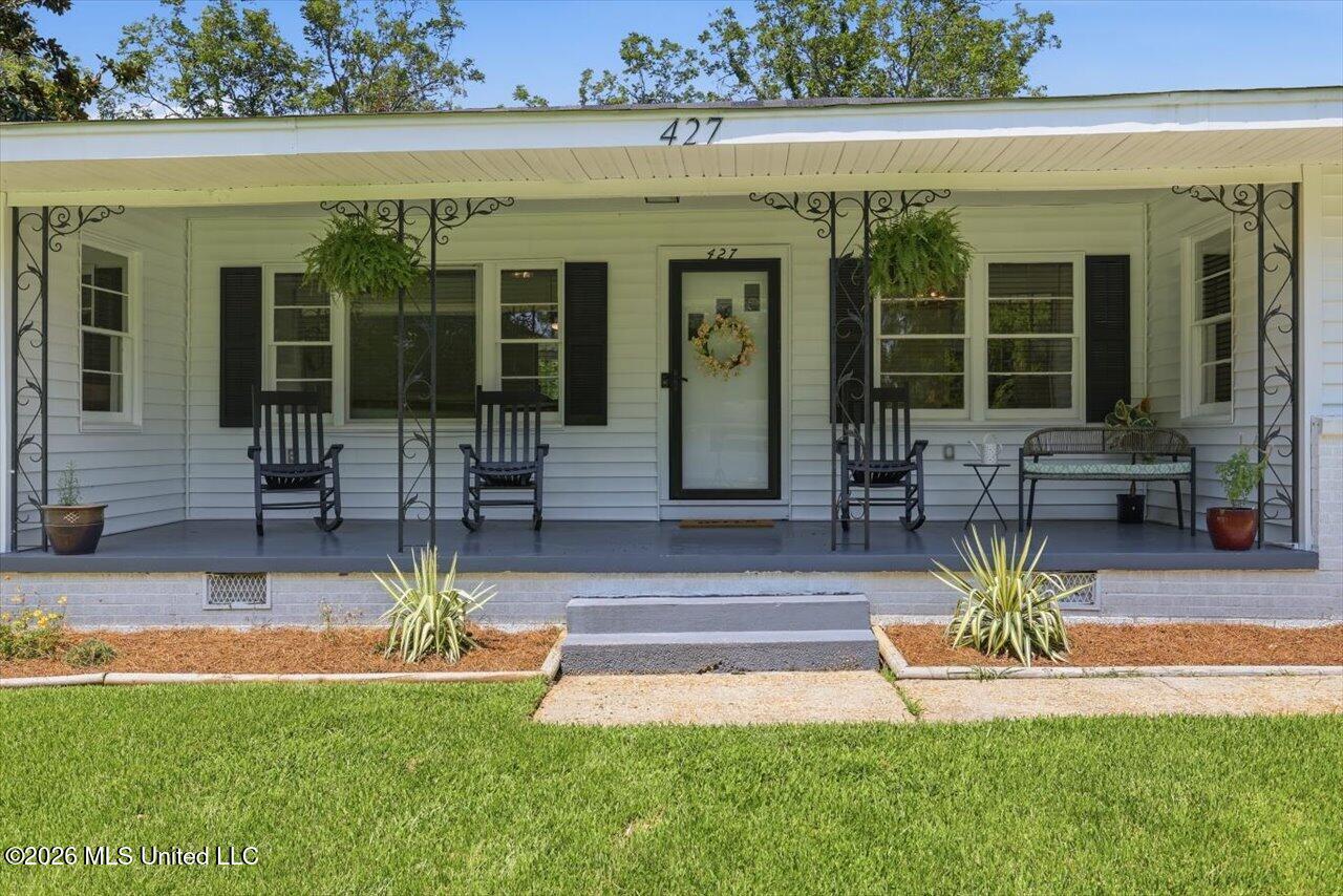 White-sided home with a covered porch, black rocking chairs, hanging ferns, and the number 427.