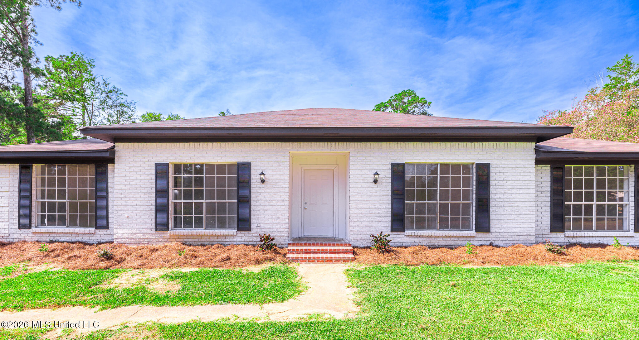 White brick single-story home with dark shutters, a centered entrance, and a broad low-pitched roof.