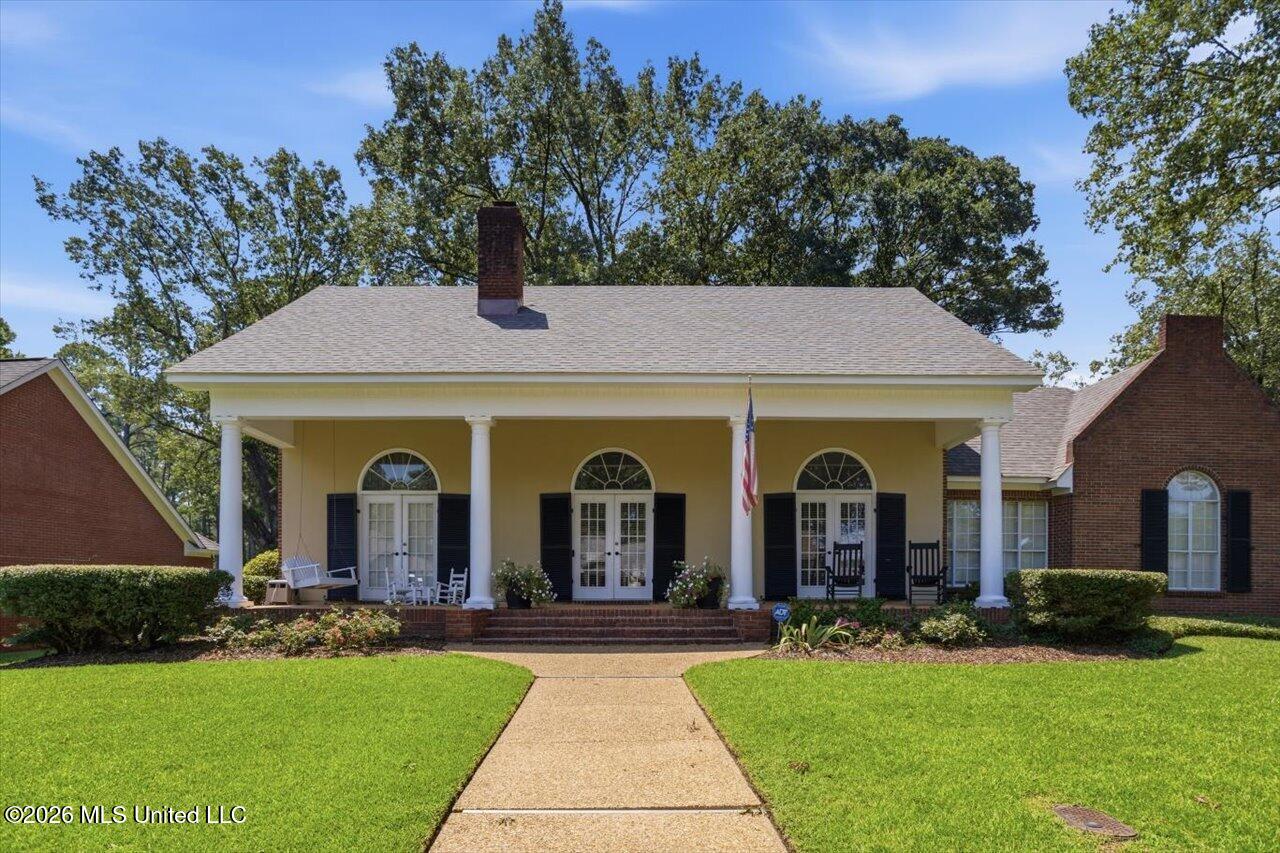 Yellow house with a columned porch, arched windows, and brick wings, viewed across a front lawn.