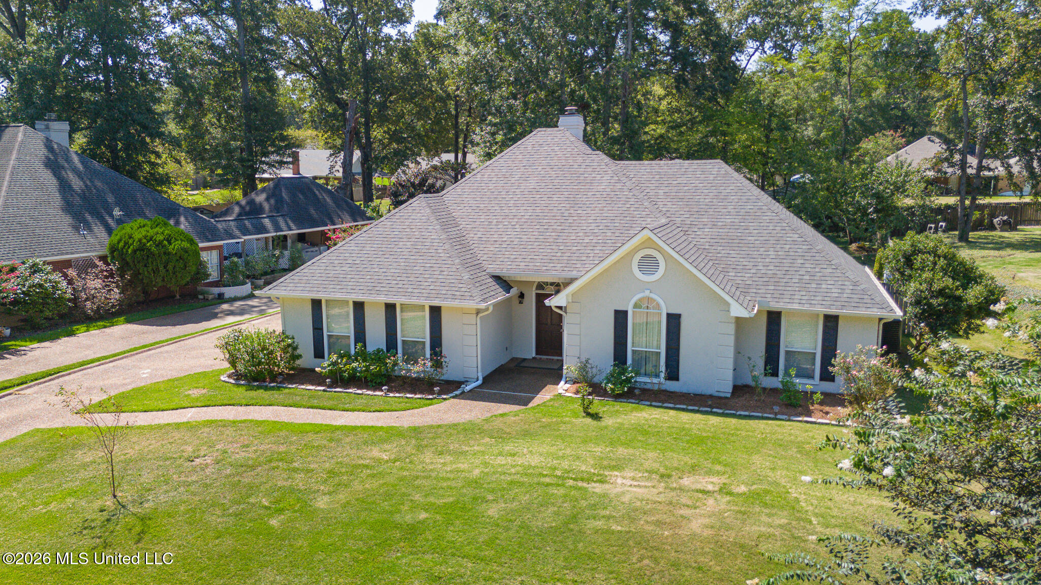 Single-story light-colored home with a gray roof, arched front window, curved walkway, and spacious lawn.