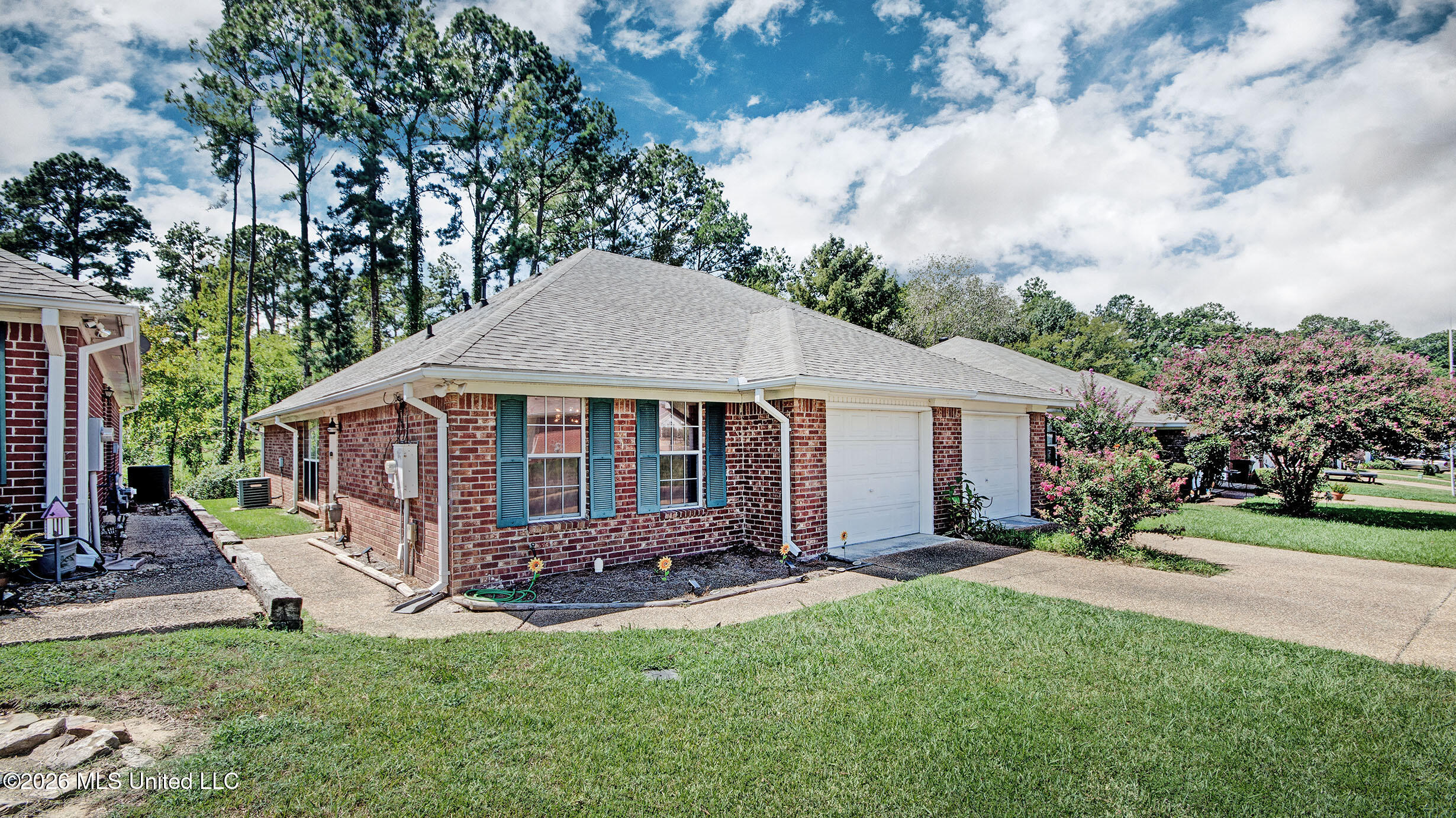Red brick home with blue-green shutters, an attached double garage, and flowering shrubs.
