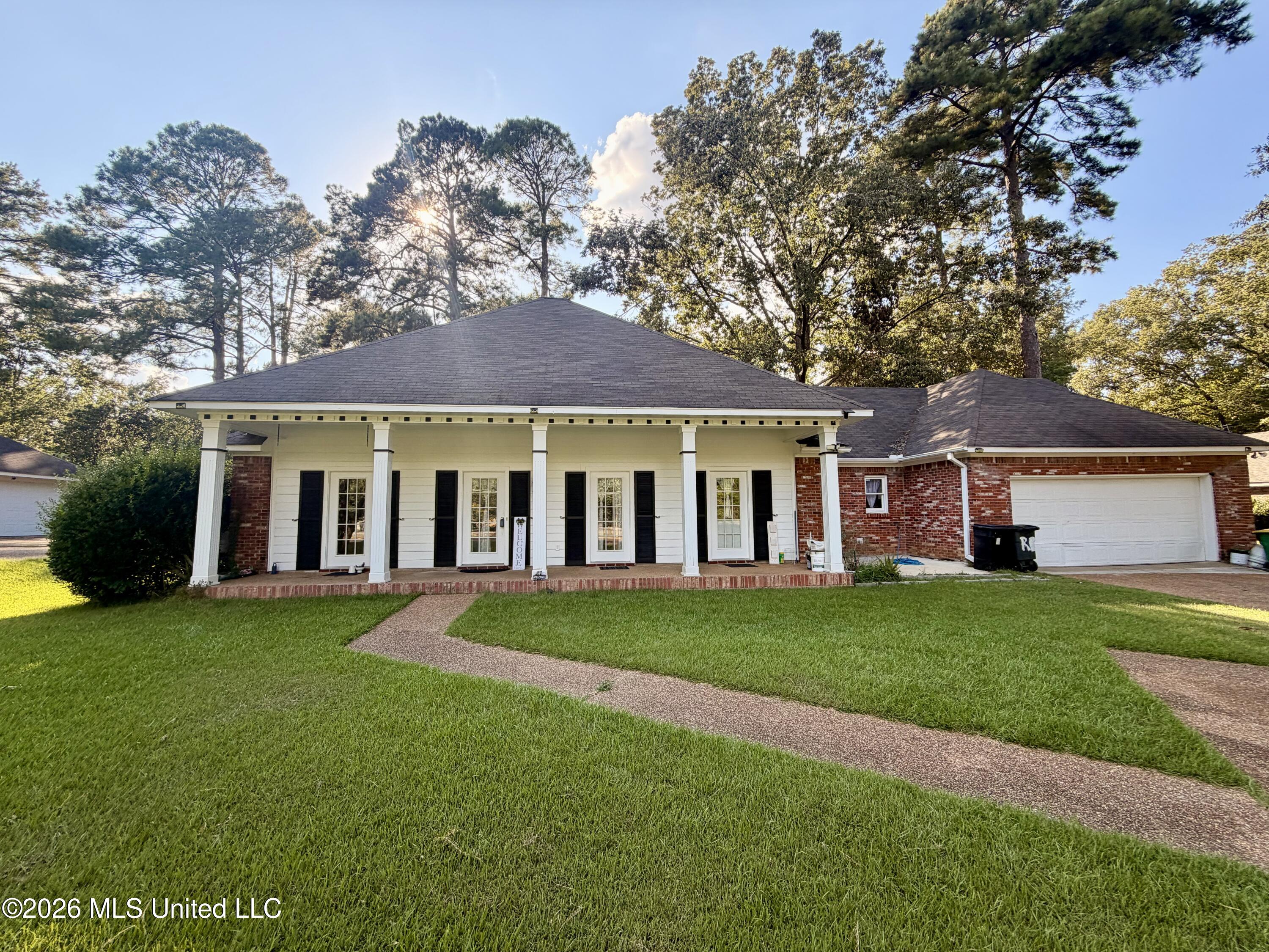Single-story home with a columned front porch, brick garage wing, and curved walkway across the lawn.