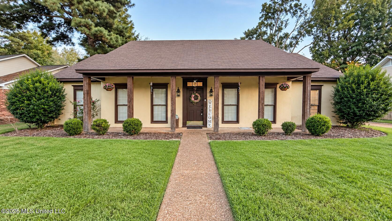 Single-story home with a broad covered porch, dark wood posts, and a walkway through the front lawn.