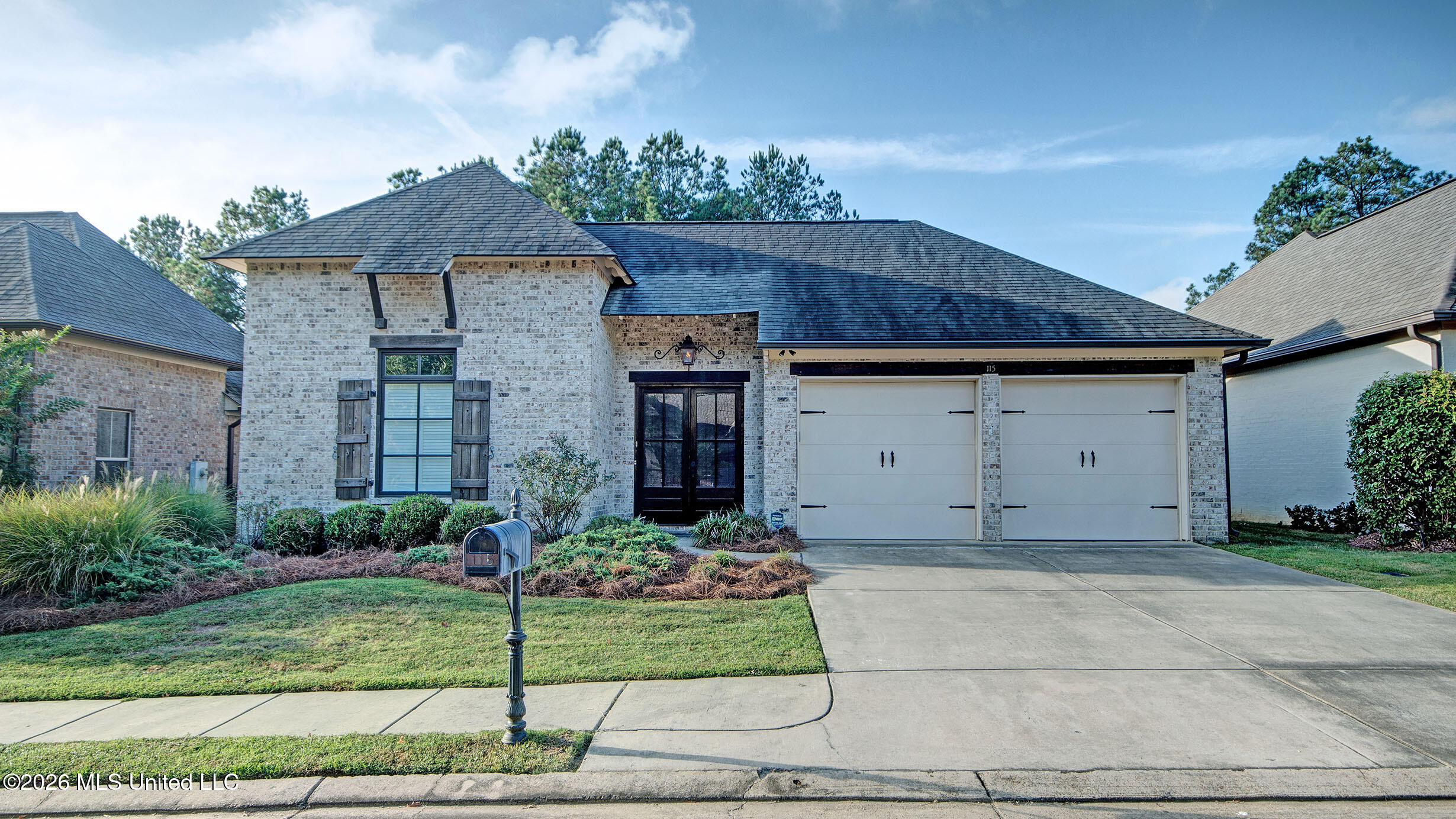 Light brick home with a two-car garage, landscaped front yard, driveway, and mailbox.