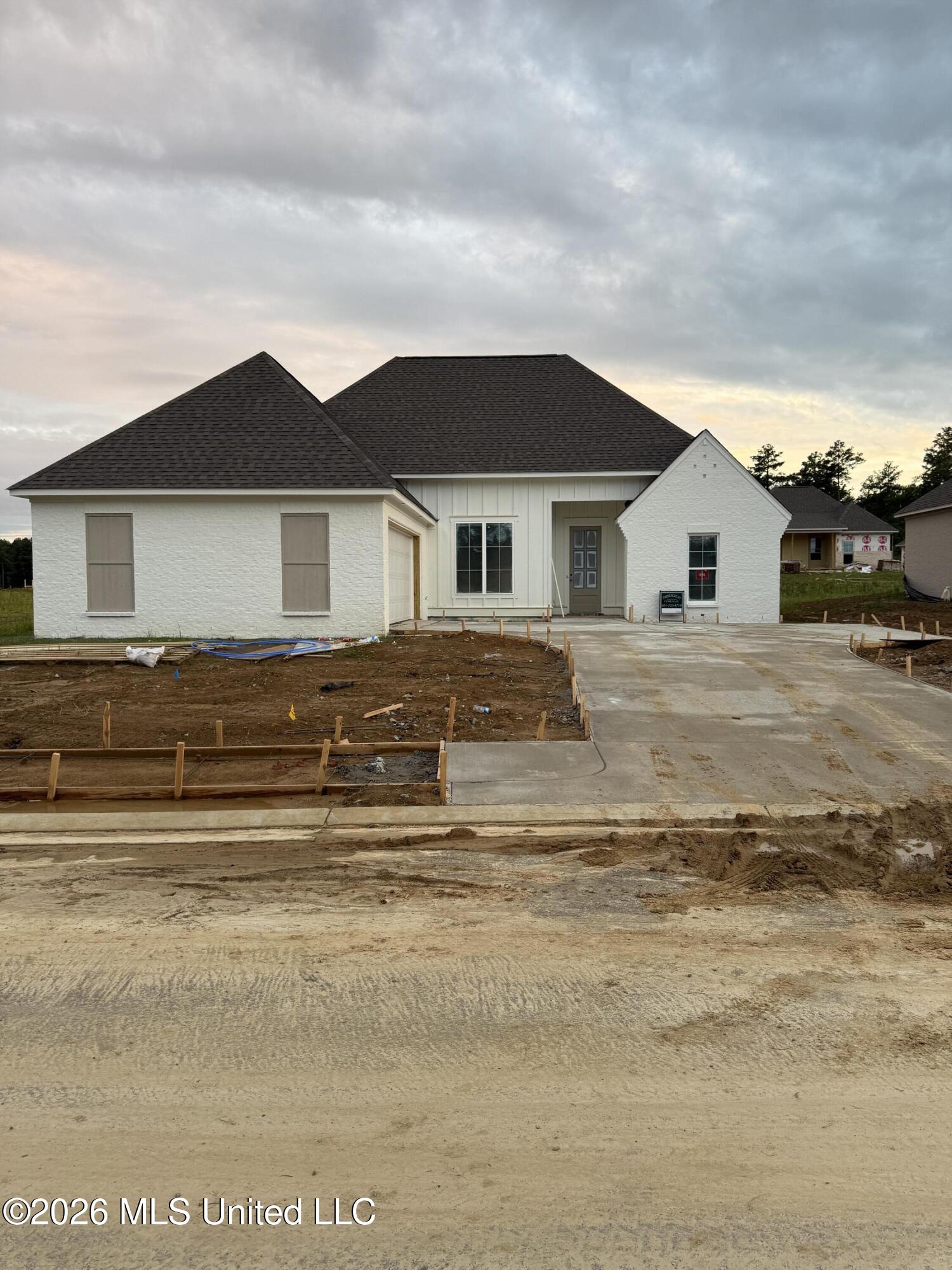 White single-story house under construction, with an unfinished dirt yard and concrete driveway.