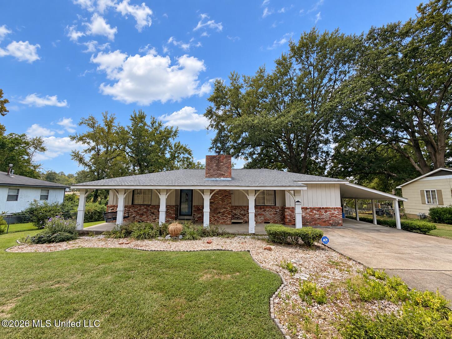 Single-story brick home with a broad covered porch, attached carport, and landscaped front lawn.
