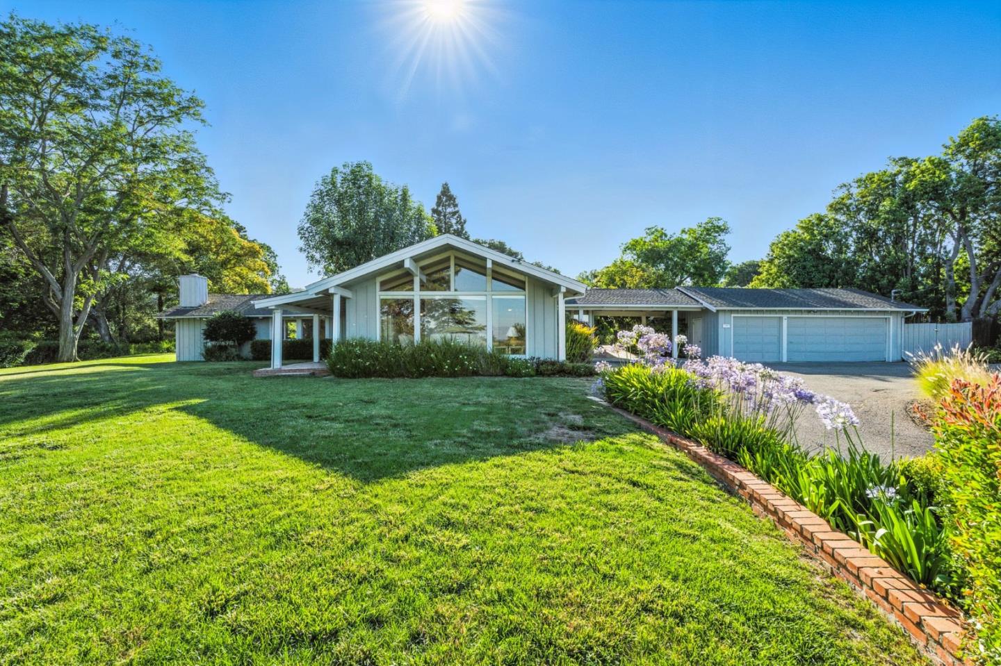 Modern home with a gabled glass facade, two-car garage, and flowering garden beds.