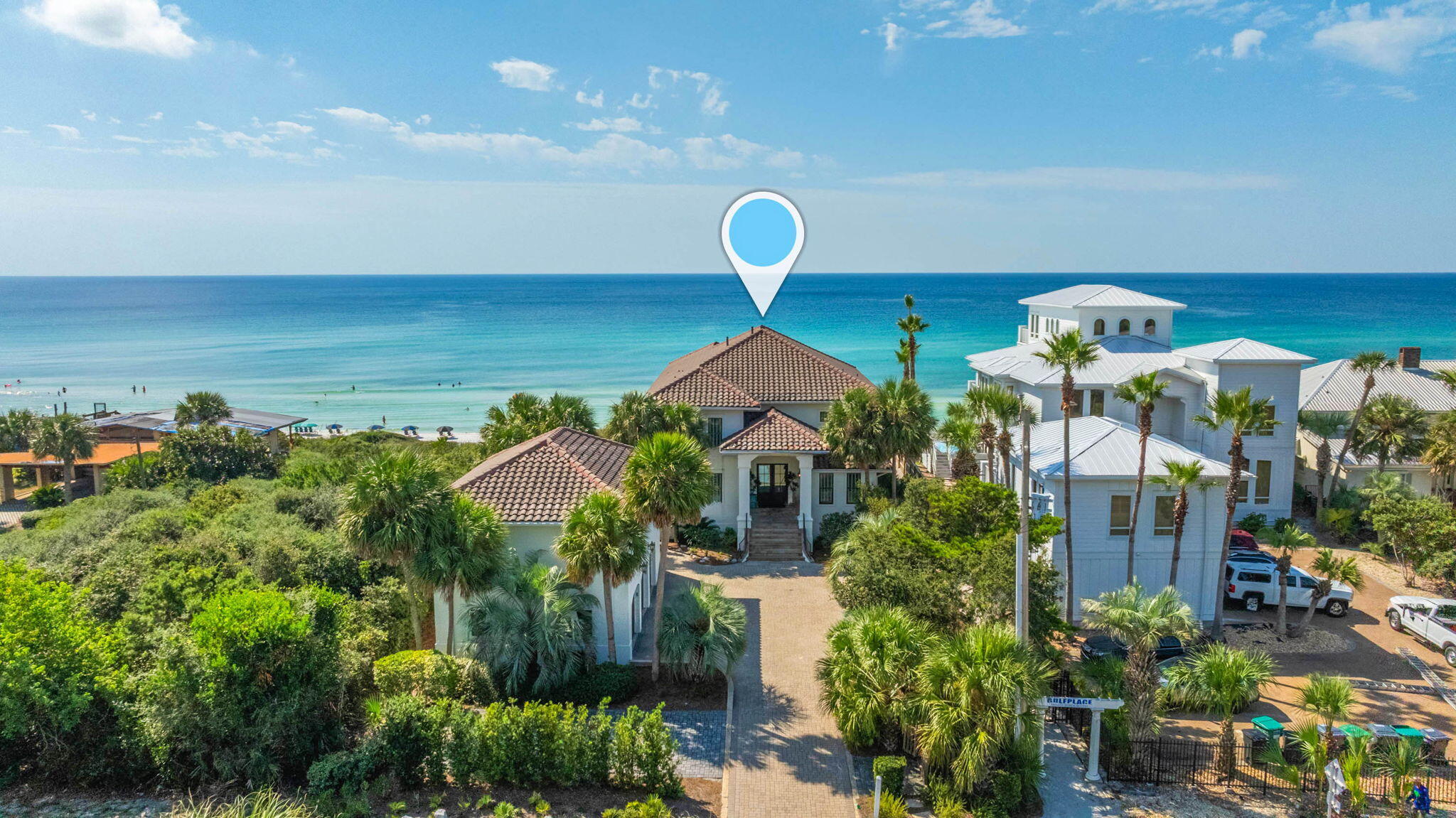 Aerial view of beachfront homes and turquoise water, with a location pin above a tile-roofed house.