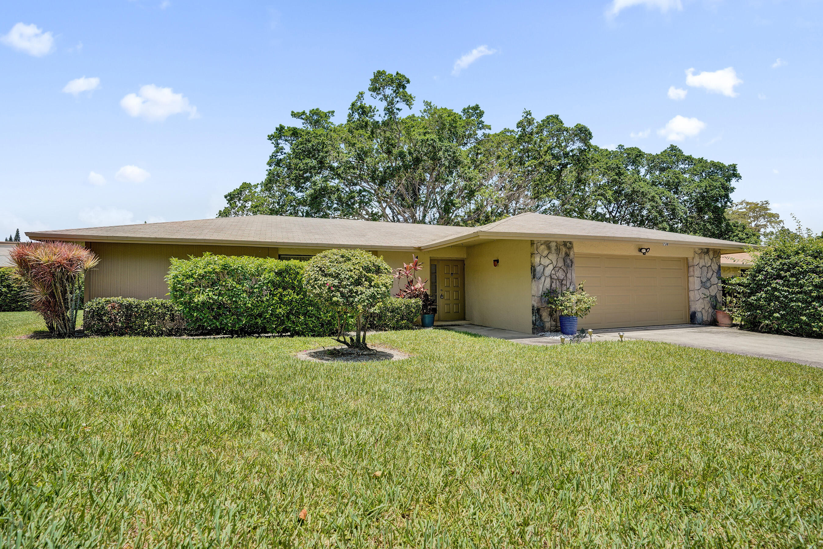 Single-story ranch house with stone garage accents, a broad lawn, and mature trees.
