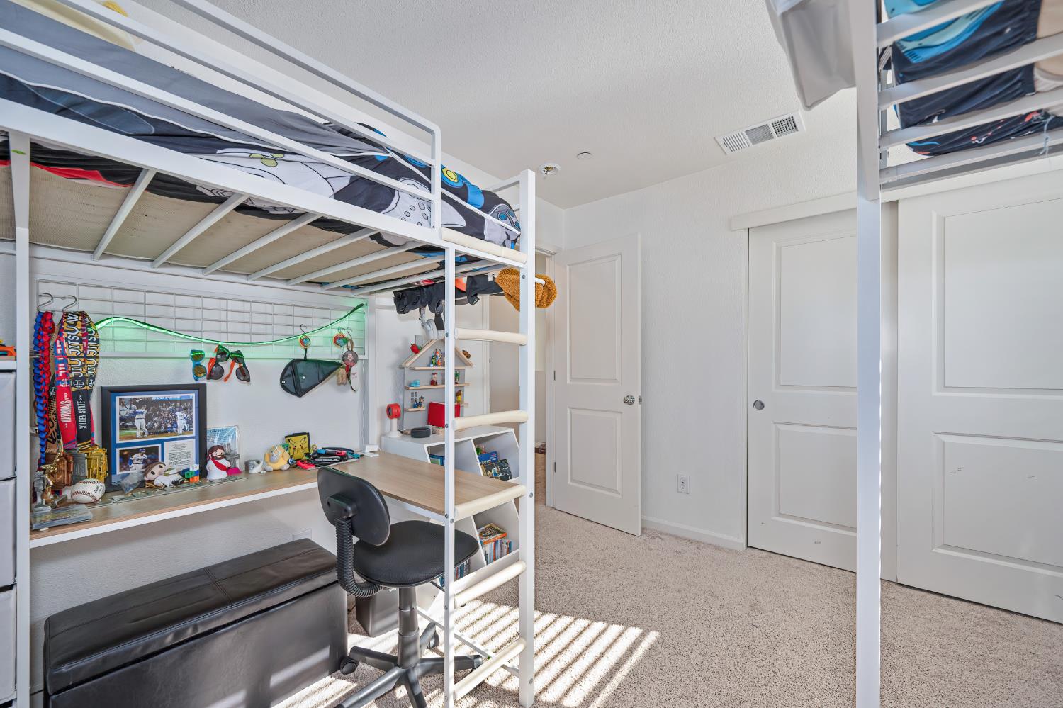 Bedroom with a white loft bunk bed, built-in desk, and sports memorabilia.