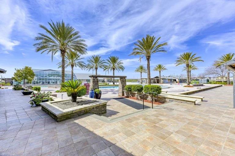 Community pool courtyard with palm trees, paved terraces, and landscaped planters.