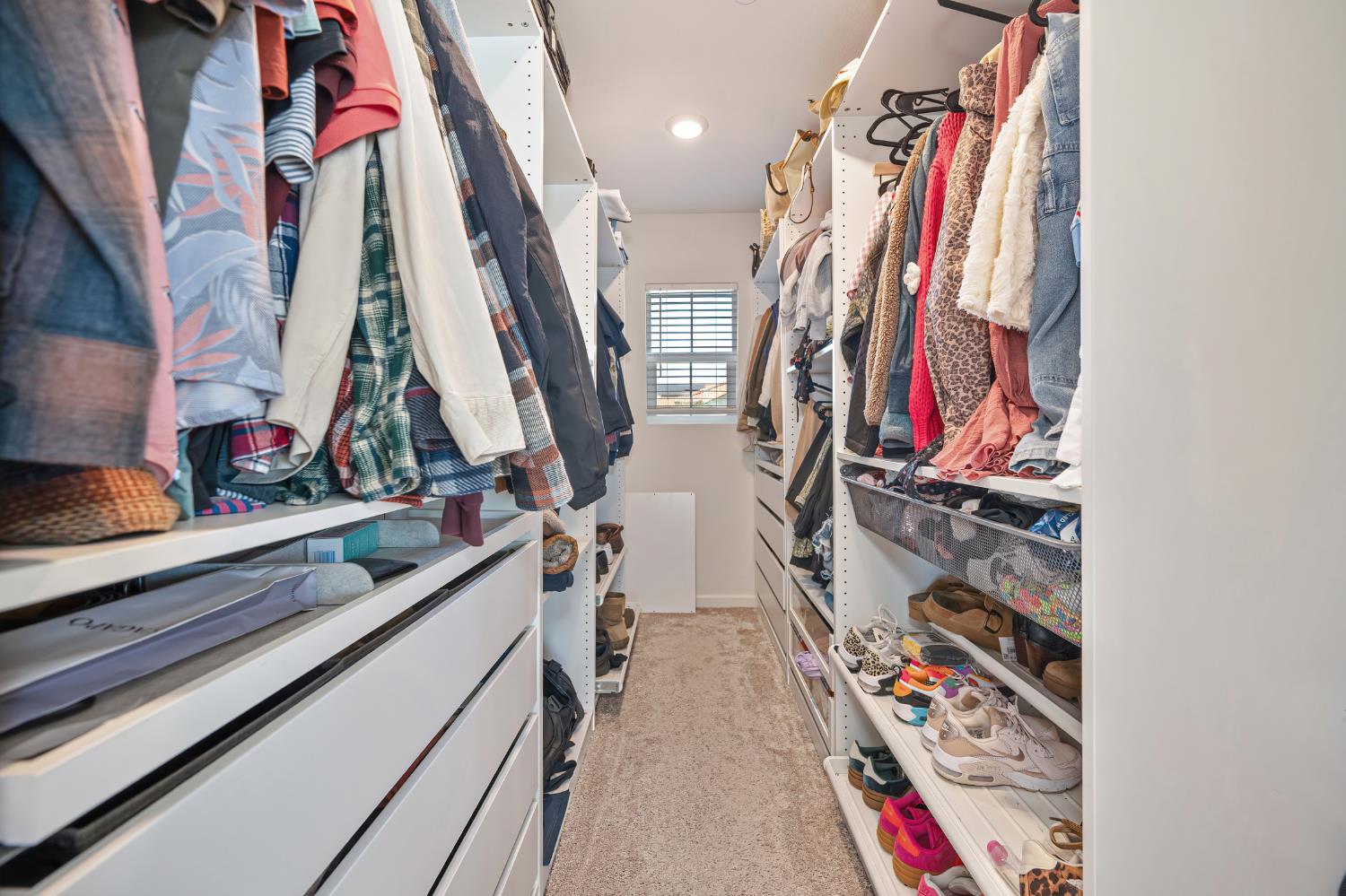 Walk-in closet with built-in drawers, clothing on both sides, and shoes lining the shelves.