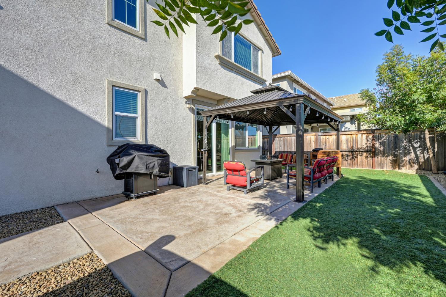 Backyard patio with a covered gazebo, outdoor dining set, grill, and lawn.