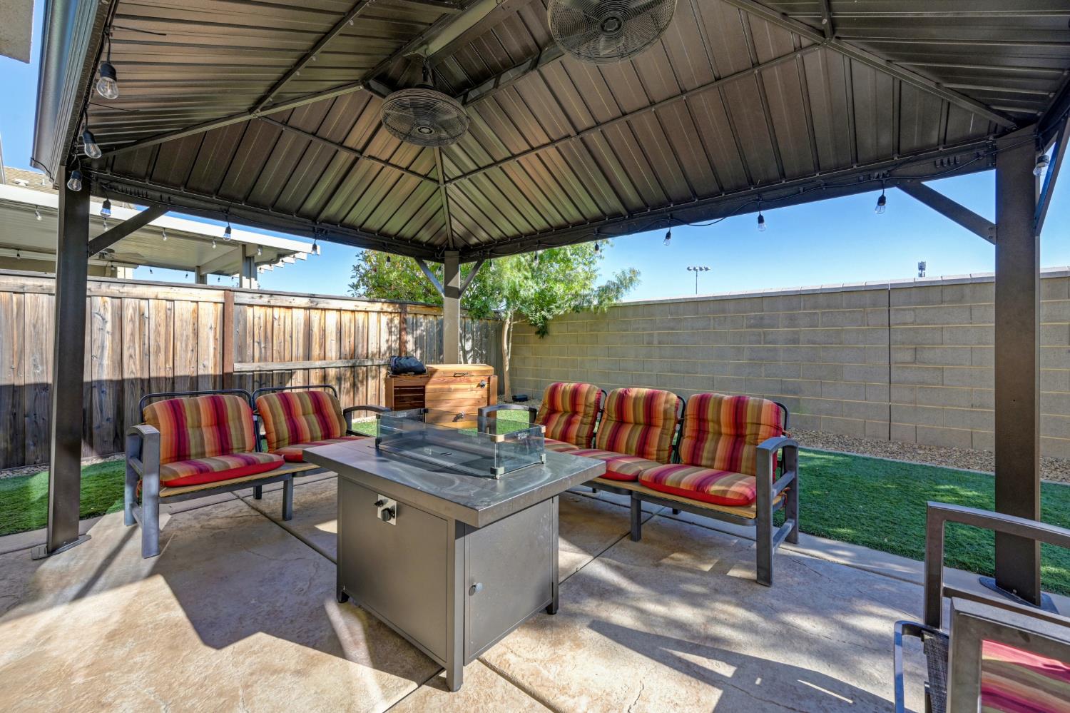 Covered backyard patio with striped seating and a fire table beneath a metal gazebo.