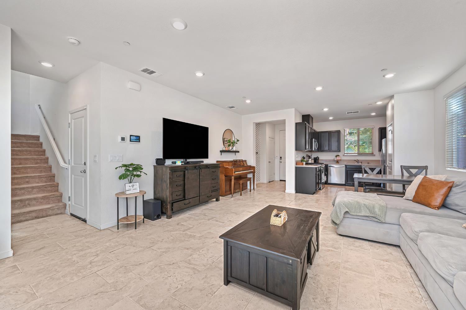 Open-plan living room with a sectional sofa, piano, and kitchen beyond.
