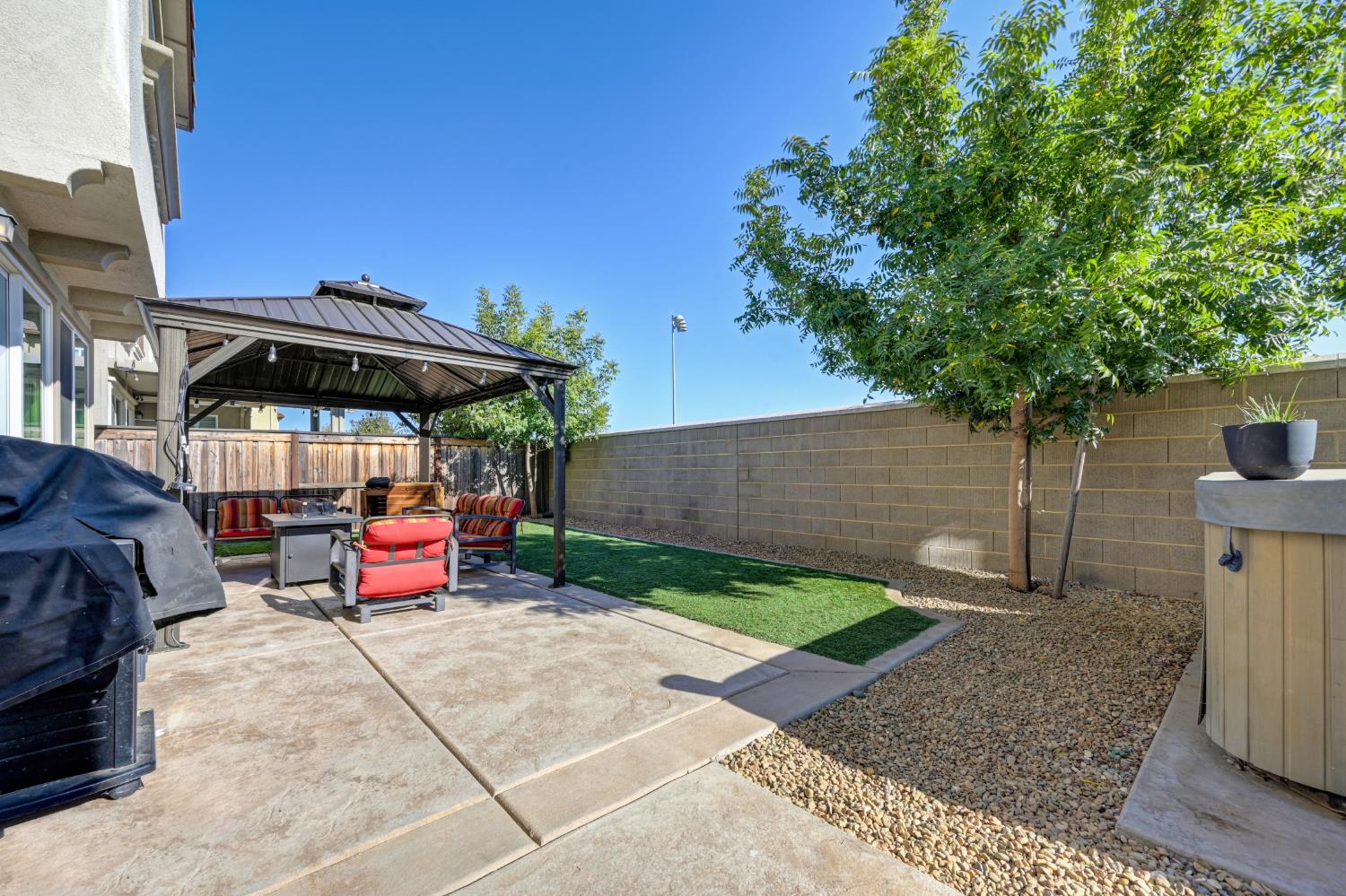 Backyard patio with a covered gazebo, colorful seating, small lawn, and gravel landscaping.