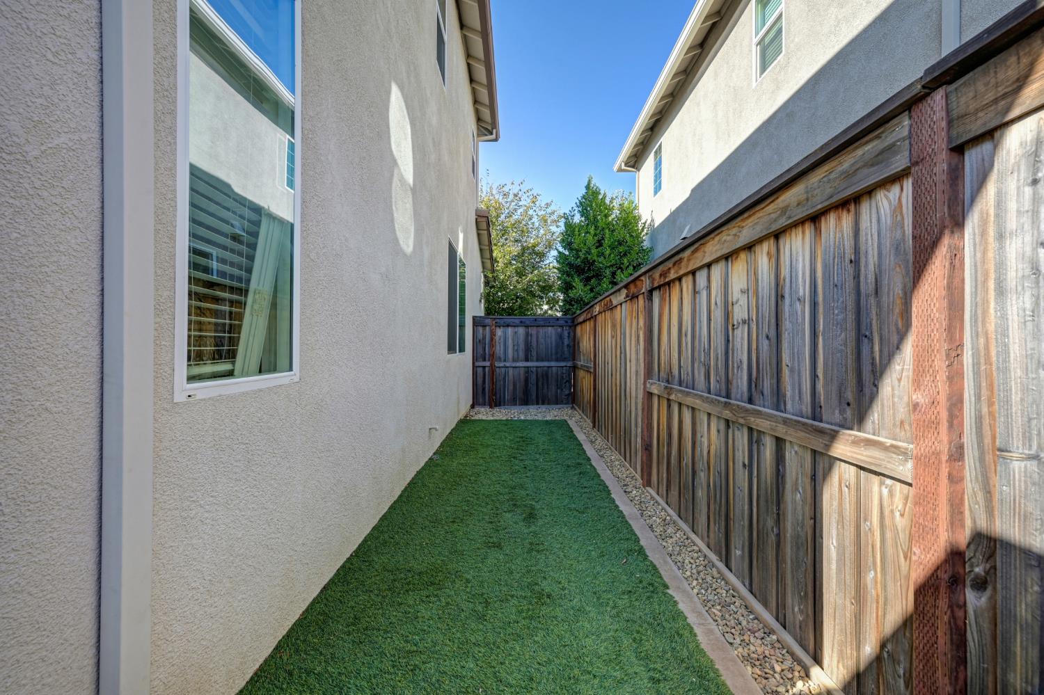 Side yard with artificial turf, a gravel border, and a tall wooden privacy fence.
