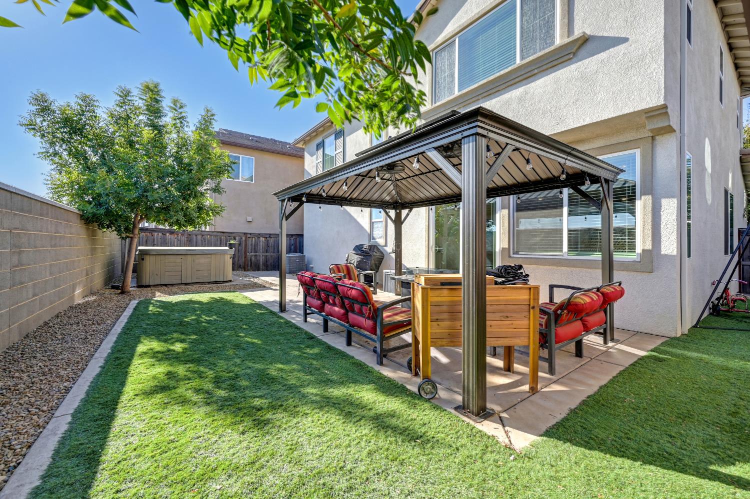 Backyard with a covered gazebo, red-cushioned seating, green lawn, and hot tub.