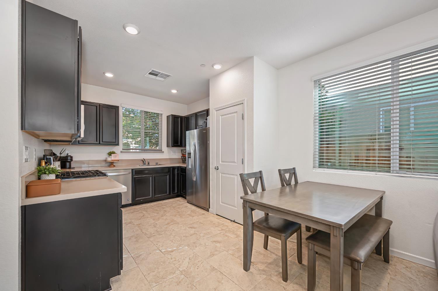 Kitchen with dark cabinets and stainless appliances, plus a dining table beside large windows.
