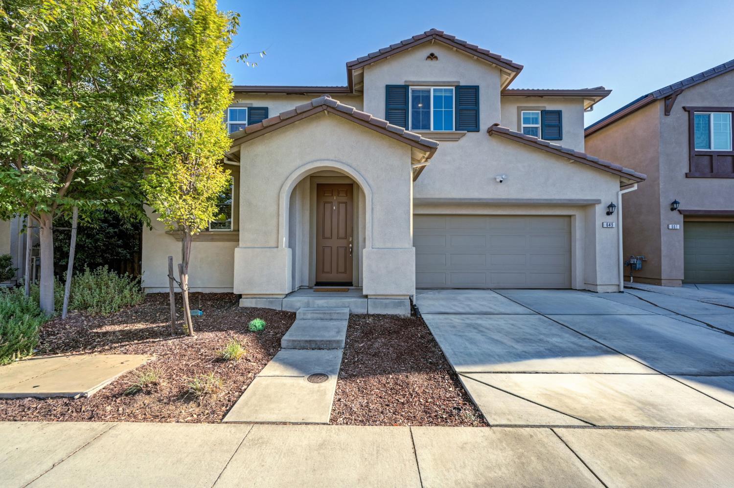 Two-story stucco home with blue shutters, an arched entry, and an attached garage.
