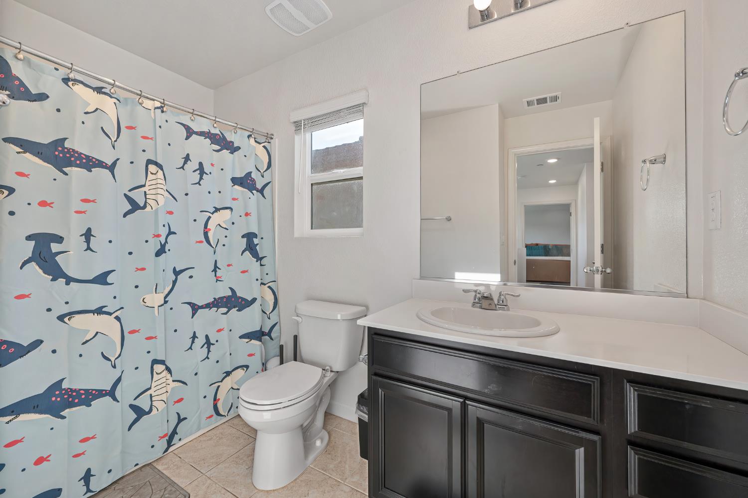 Bathroom with a sea-creature shower curtain, dark vanity, white toilet, and large mirror.