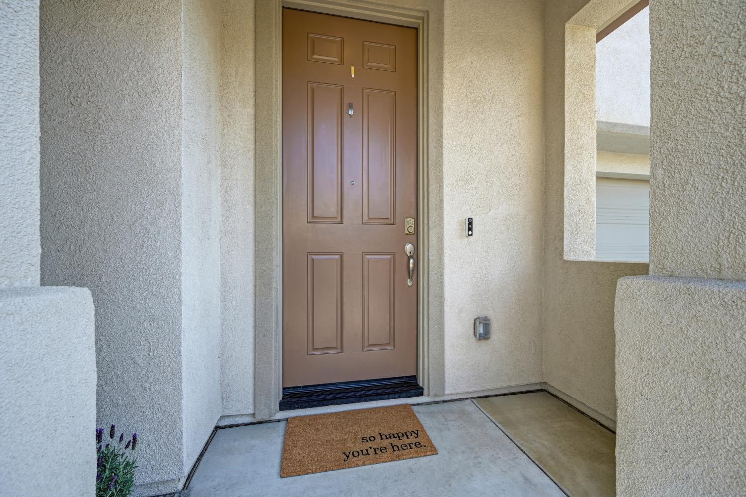 Covered front entry with a brown paneled door and a welcome mat.