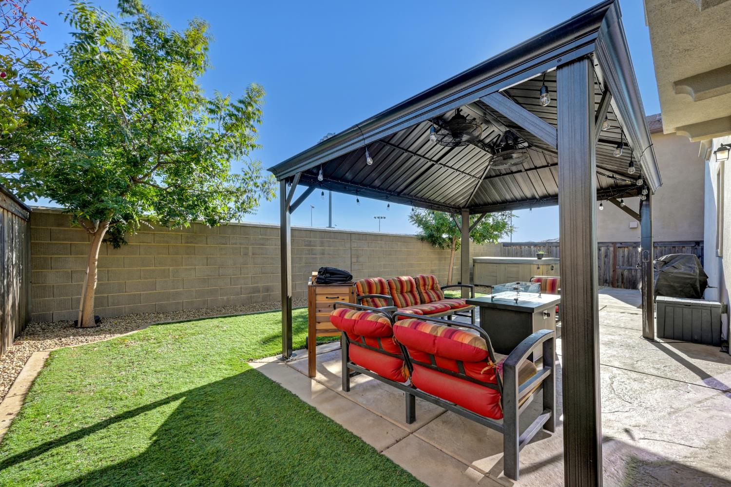 Backyard patio with a metal pavilion, colorful cushioned seating, fire table, and hot tub.