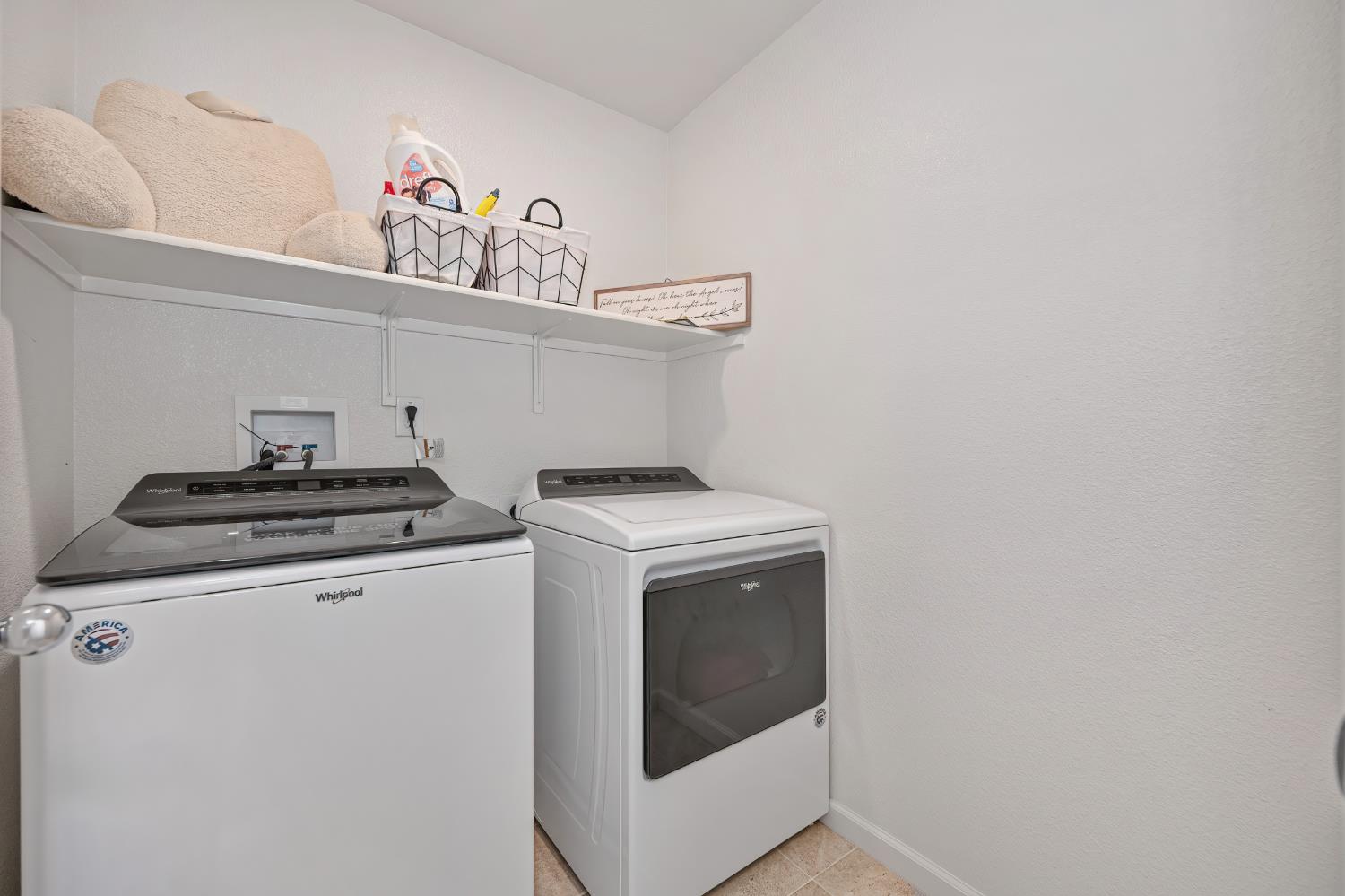 Laundry room with a top-loading washer, front-loading dryer and storage shelf above.