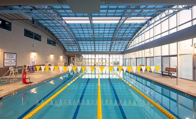 Indoor lap pool with yellow lane dividers beneath a glass roof and large windows.