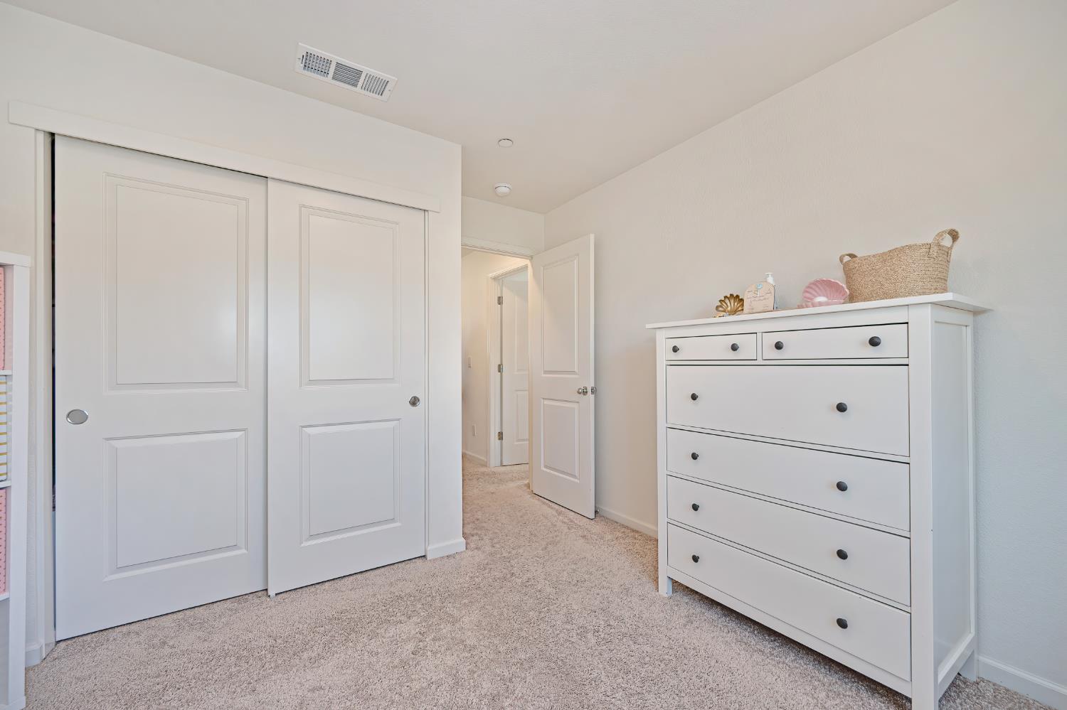 Bedroom with white sliding closet doors, beige carpet, and a white dresser.