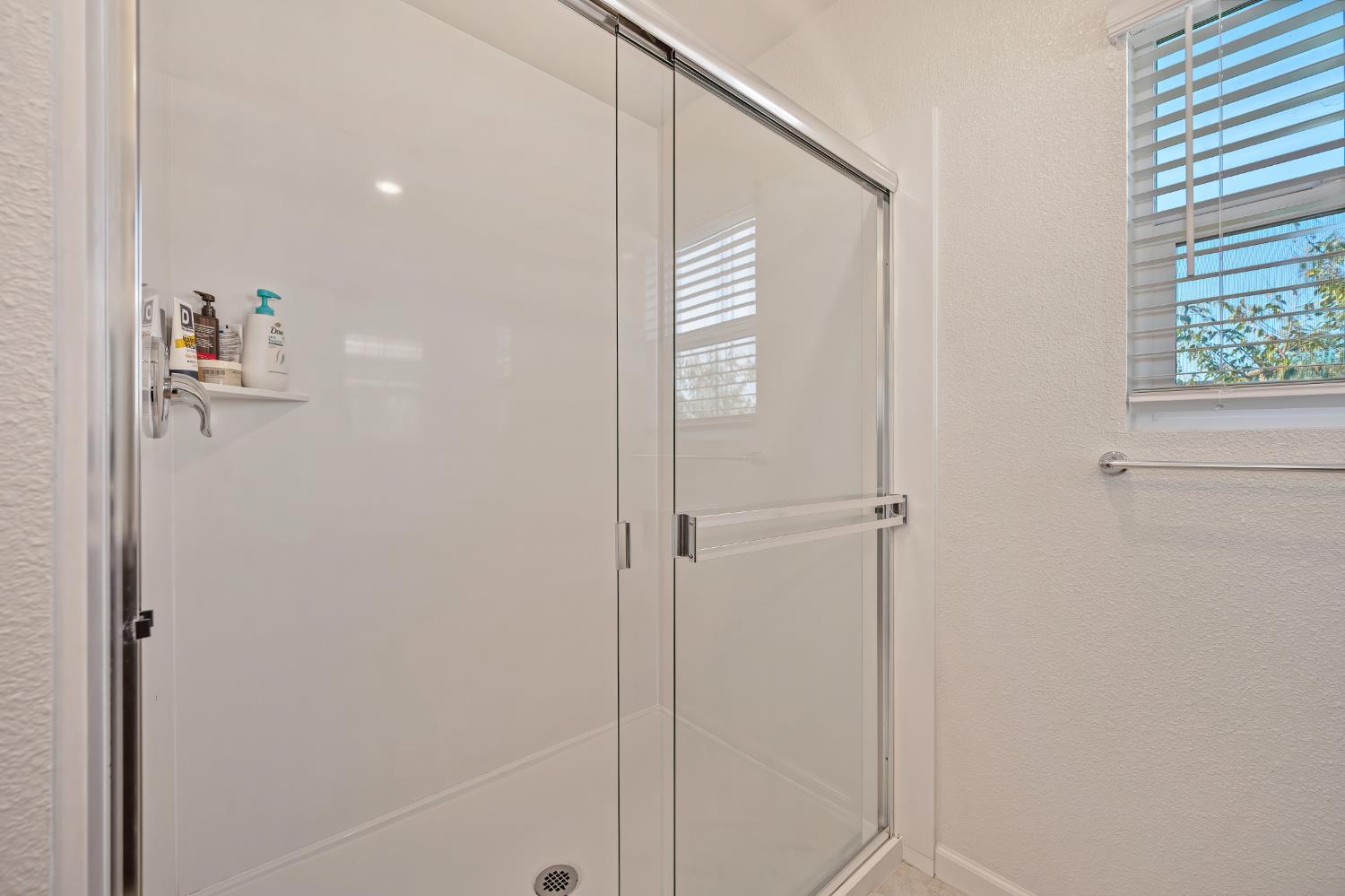 Bathroom shower with a clear glass sliding enclosure and a window with horizontal blinds.