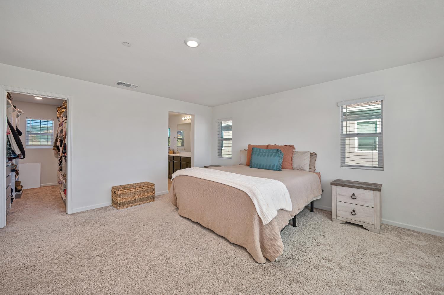 Staged bedroom with a large bed, walk-in closet, and adjoining bathroom doorway.