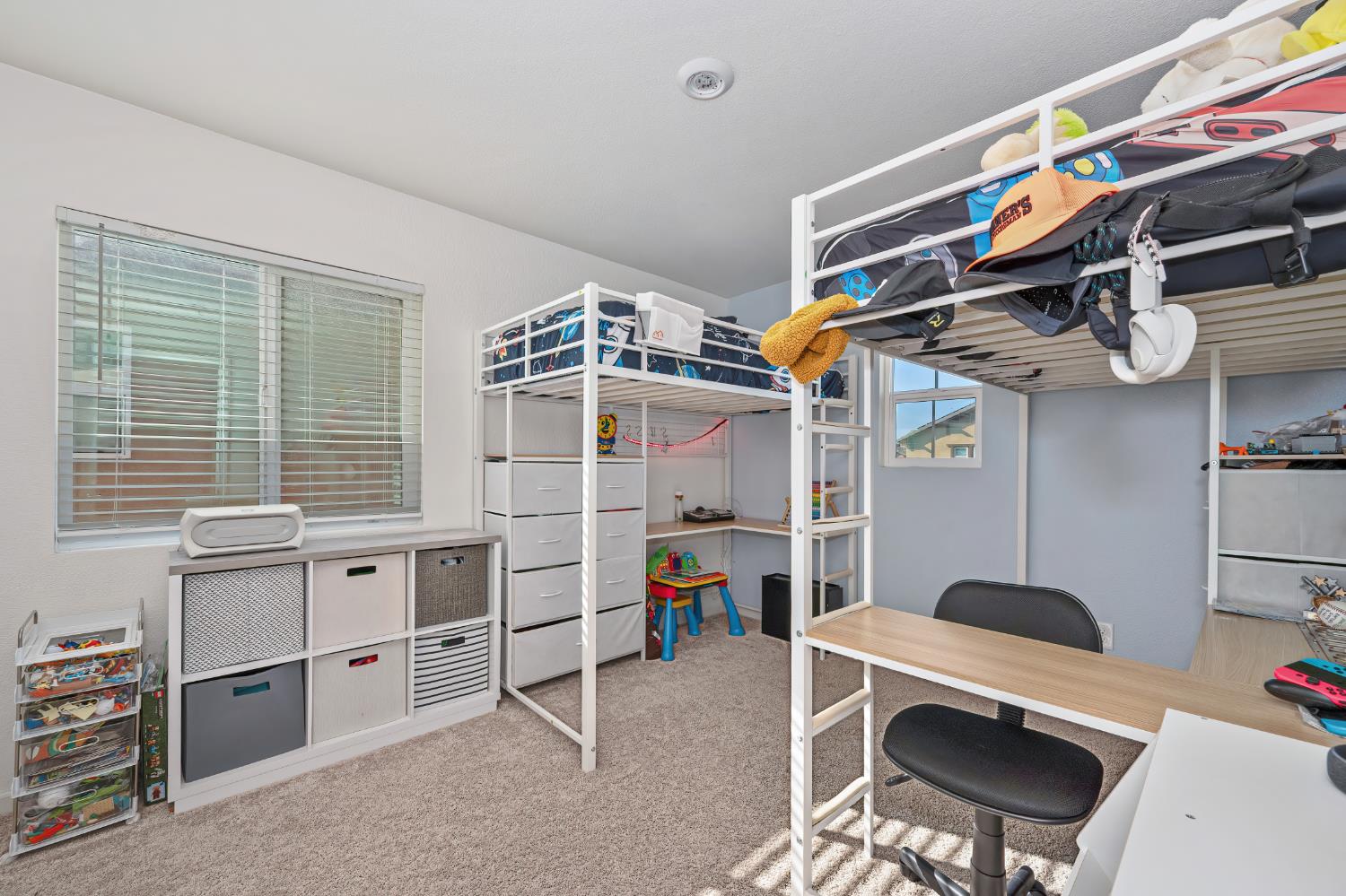 Bedroom with two white loft bunk beds, a desk, and storage furniture.
