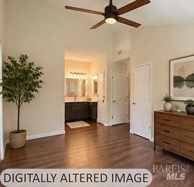Bedroom with wood flooring, ceiling fan, closet doors, and an open view to the bathroom vanity.