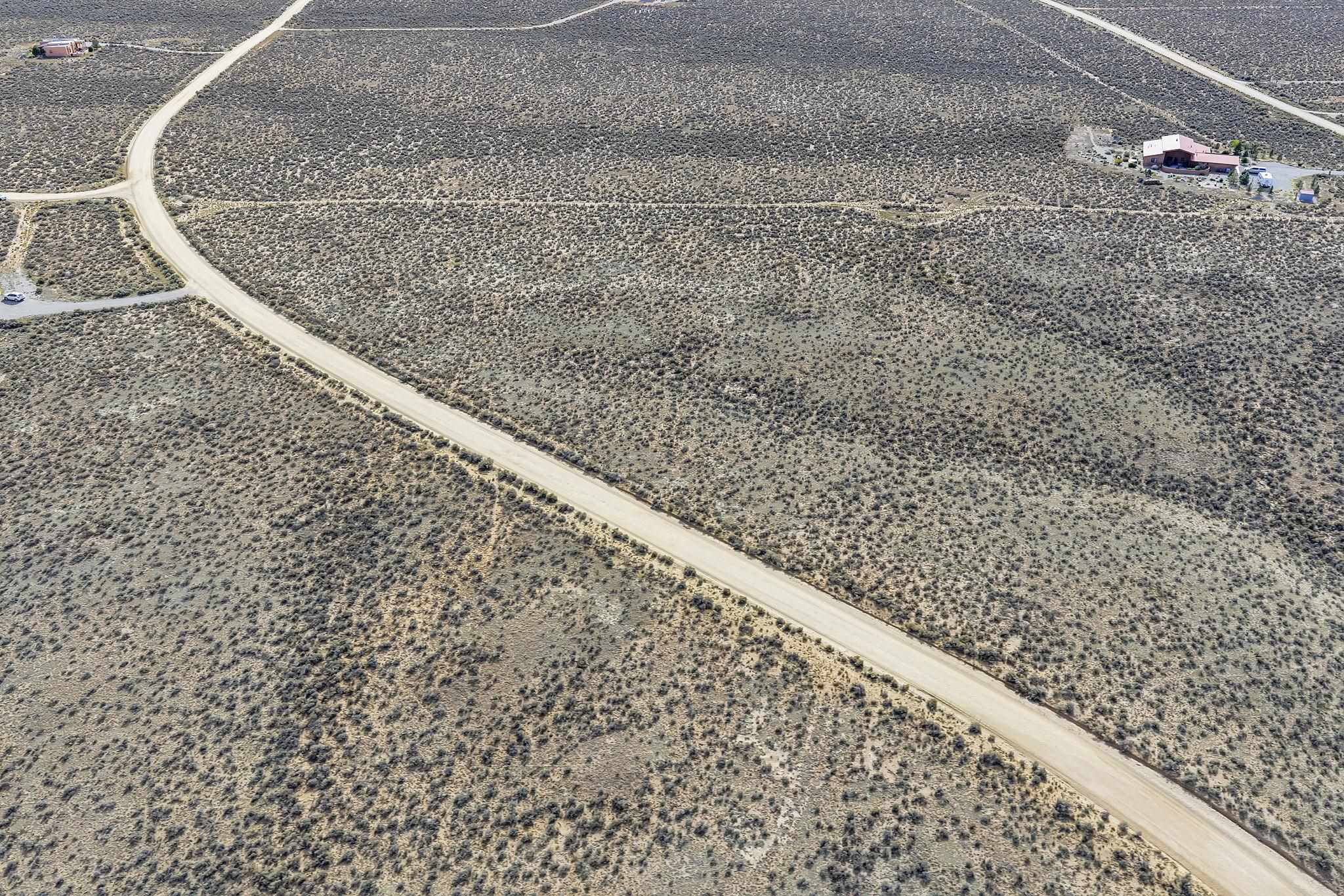 Aerial view of vacant scrubland crossed by unpaved roads, with homes nearby.
