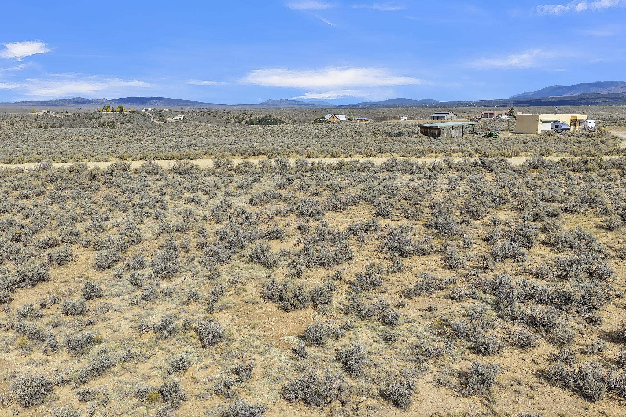 Open sagebrush land with a dirt road, distant buildings, and mountain views.