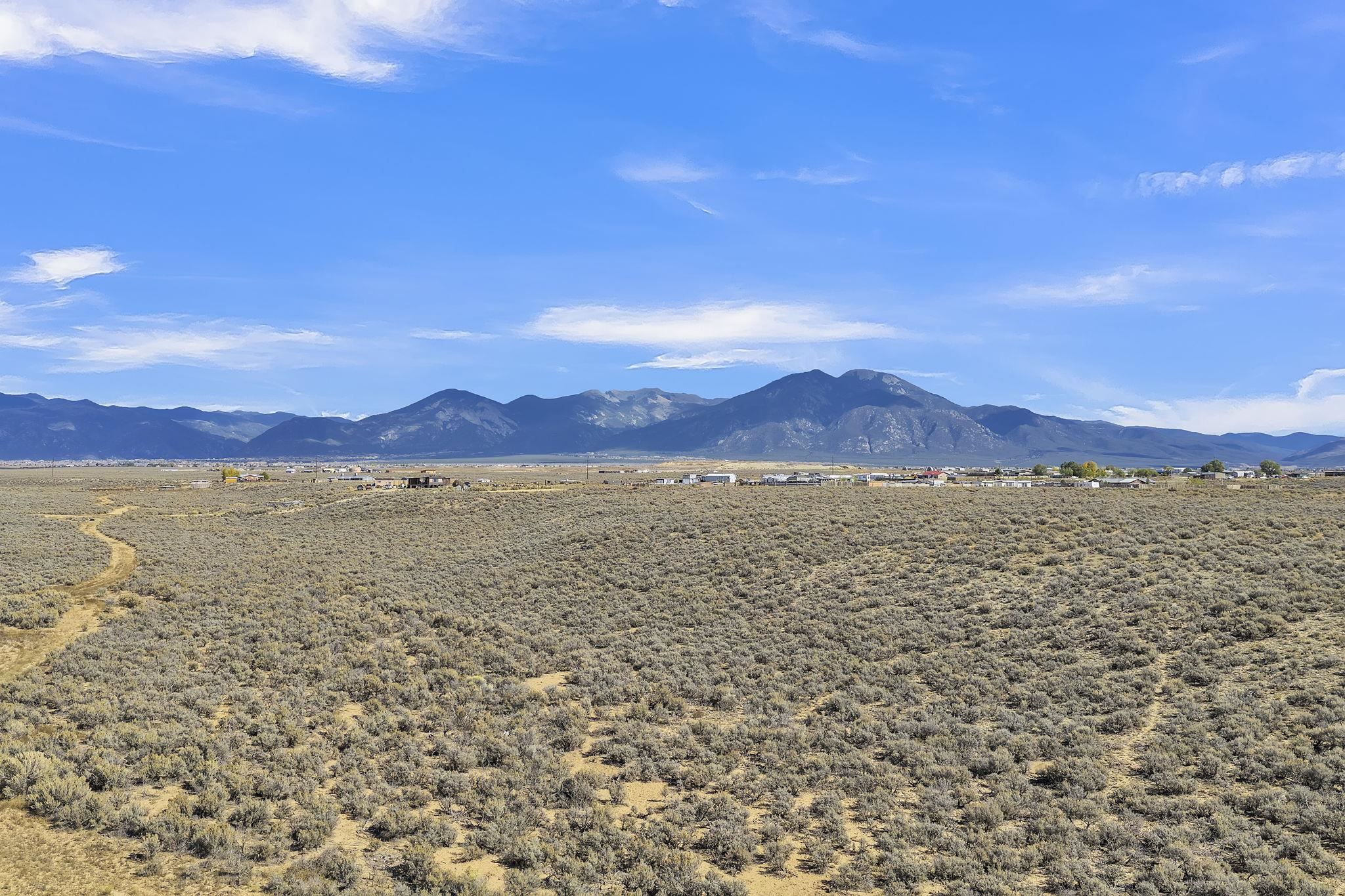 Vacant sagebrush land with dirt tracks and a wide view of distant mountains.