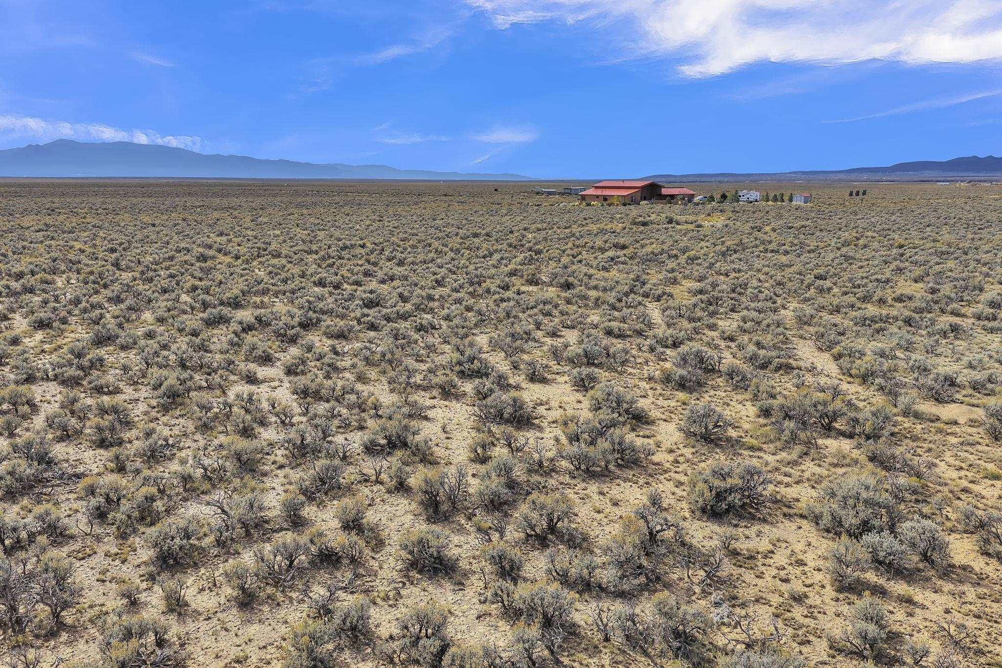 Aerial view of scrub-covered acreage with a distant red-roofed home and mountain range.