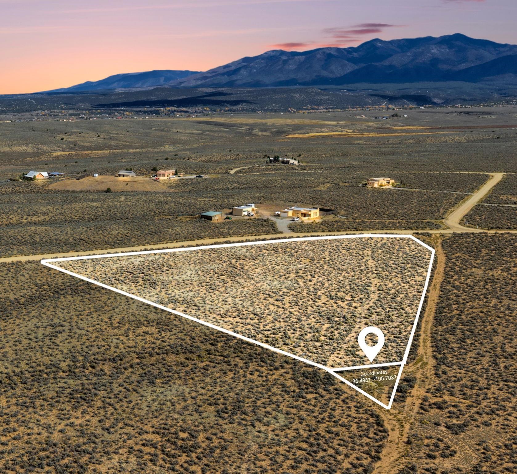 Aerial view of a scrub-covered parcel outlined beside a dirt road, with mountains in the distance.