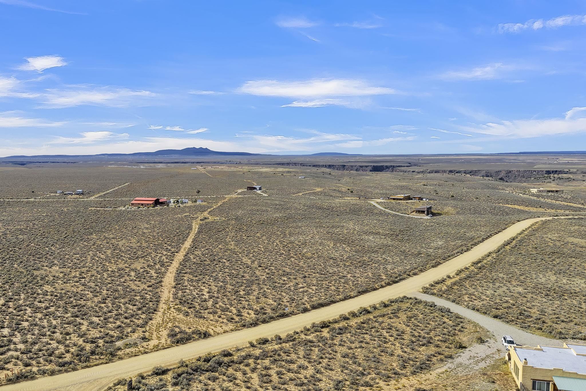 Aerial view of open scrubland, dirt roads, scattered homes, and distant low mountains.