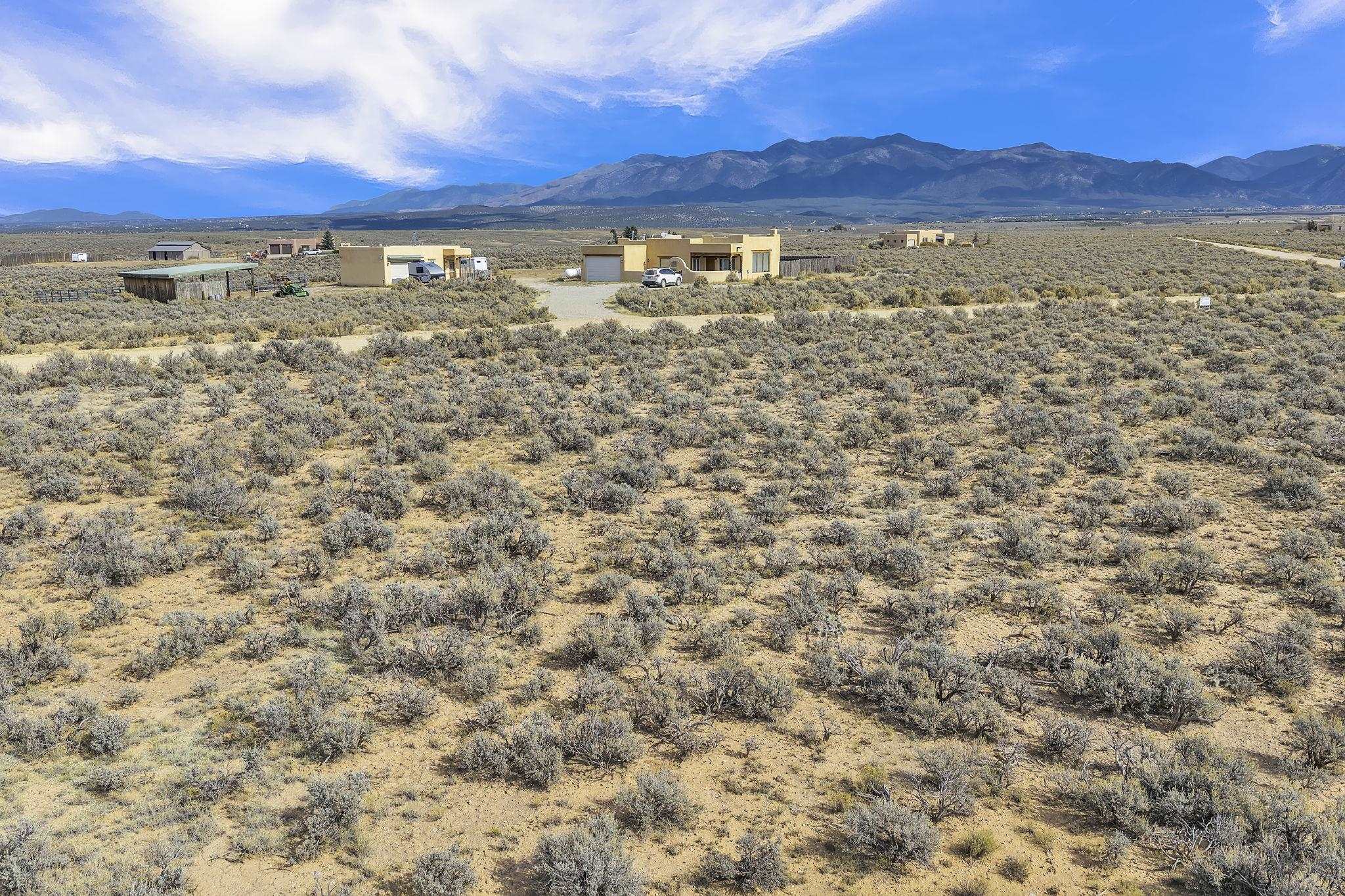 Aerial view of sagebrush-covered land with distant homes and mountains.