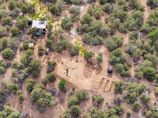 Aerial view of a brush-covered lot with a broad clearing, small outbuilding, and water tank.