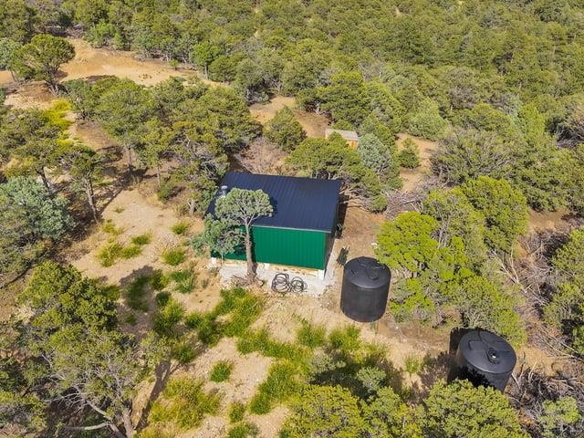 Aerial view of a green metal shed and water tanks among wooded, dry terrain.