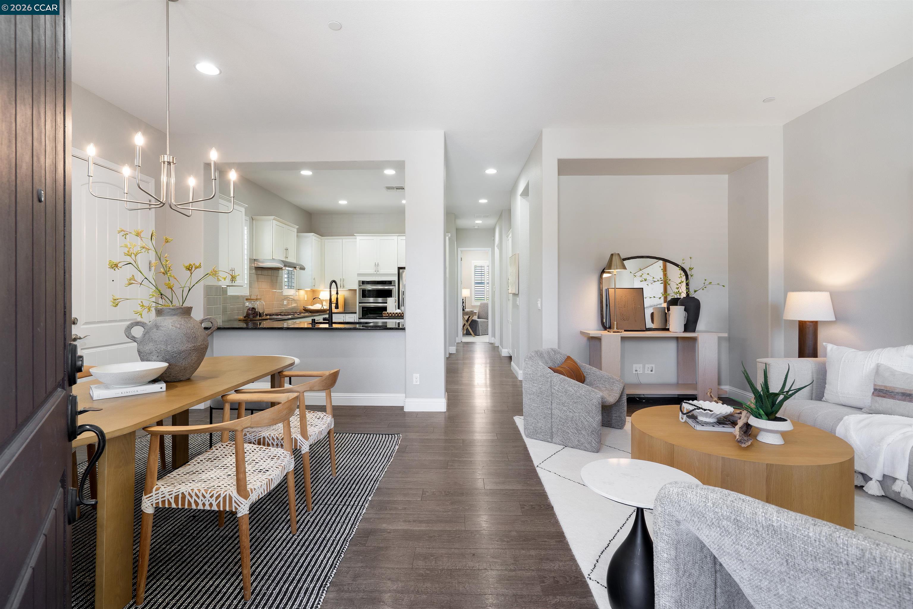 Open-plan dining and living area with a white kitchen, wood floors, and contemporary furnishings.