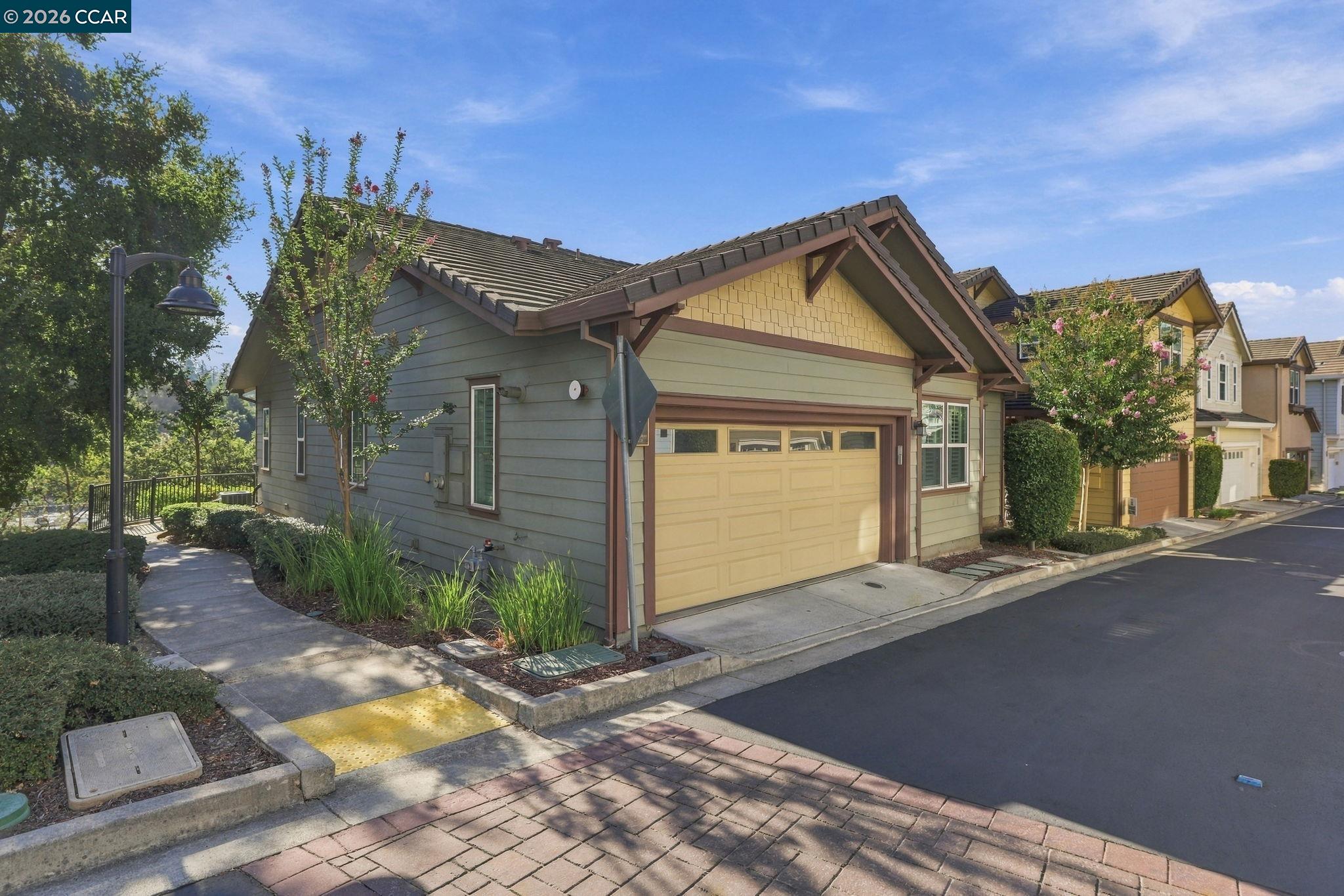 Gabled house with a yellow garage door beside a landscaped sidewalk and neighboring homes.