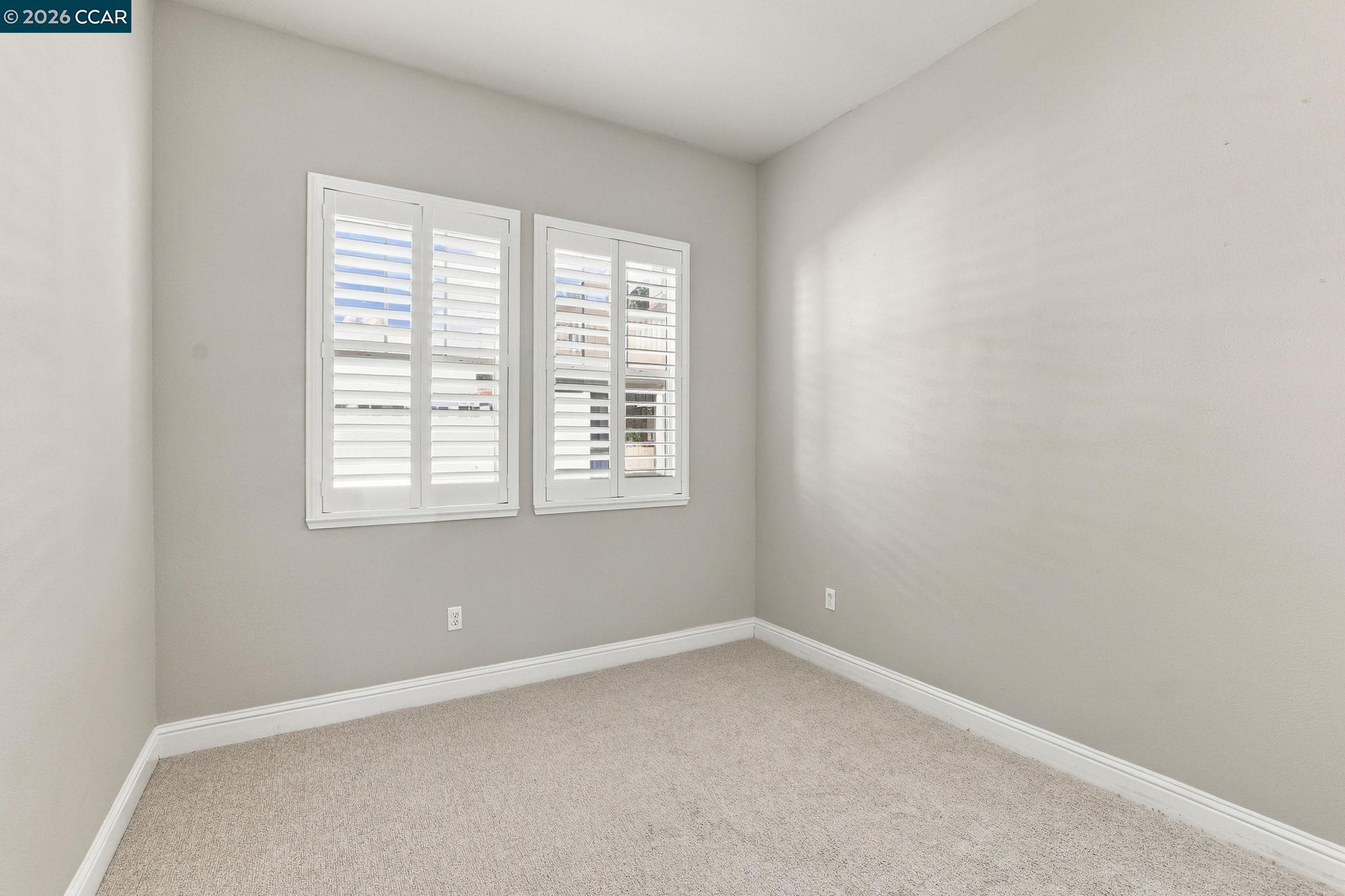 Empty carpeted room with two windows fitted with white plantation shutters.