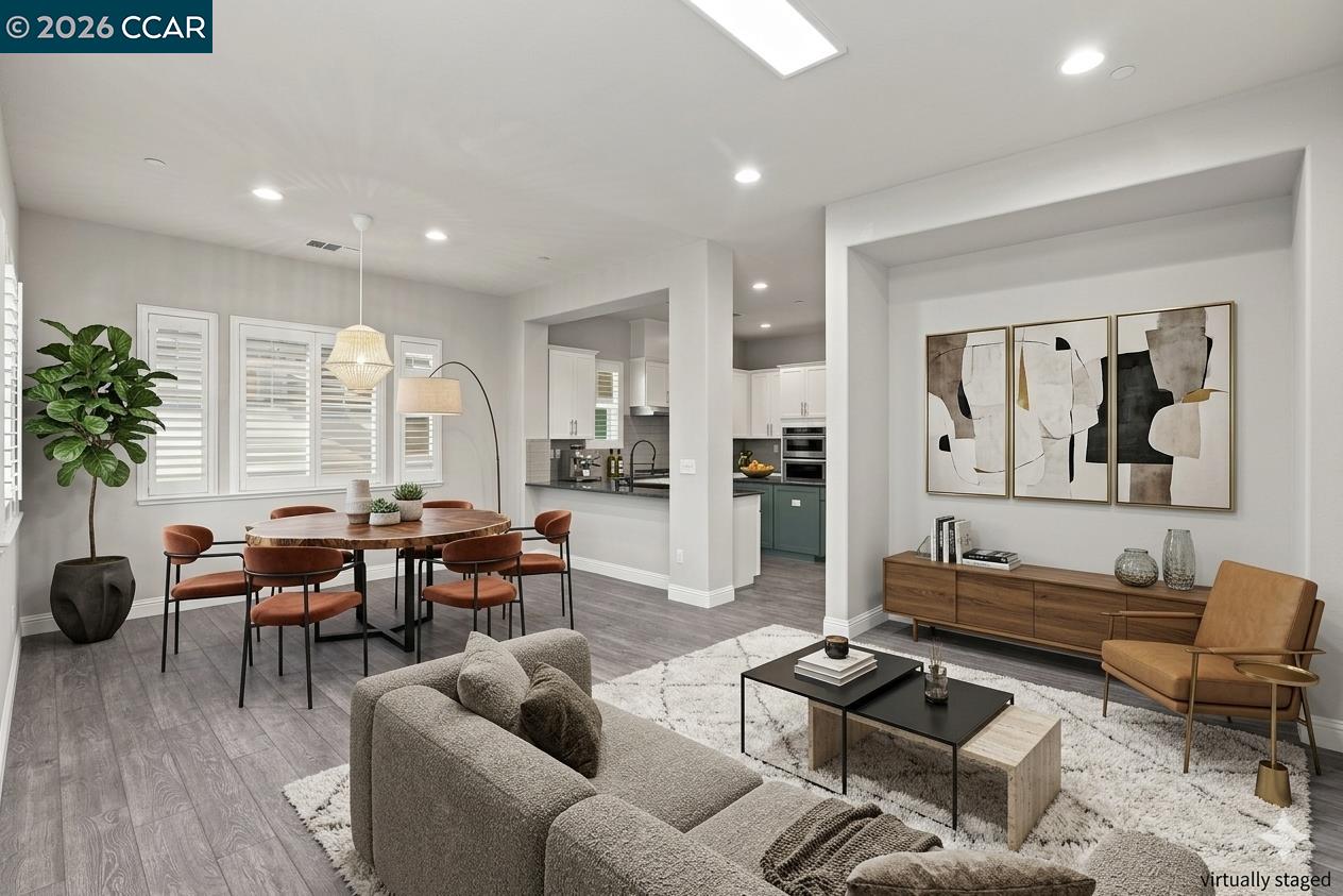 Open-concept living and dining area with a gray sofa, wood dining table, and kitchen beyond.