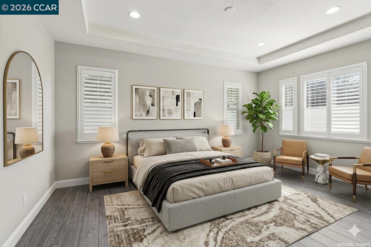 Staged bedroom with a large upholstered bed, shuttered windows, abstract artwork, and a potted plant.